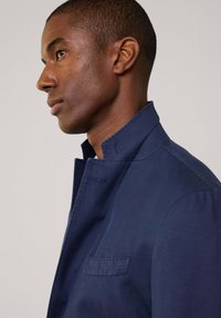Granatowa kurtka z kołnierzem, wykonana z gładkiej bawełny, charakteryzująca się eleganckim fasonem, jedną kieszenią i subtelnymi detalami w szwach.