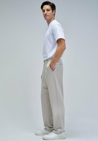 Pantalones de pierna ancha en gris claro con una tela texturada y bolsillos frontales, combinados con una camiseta blanca lisa y zapatillas blancas.