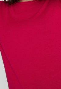 Getailleerde top met korte mouwen in felroze stof, gladde textuur, met een ronde halslijn en subtiele stretch. Geen zichtbare patronen of hardware.