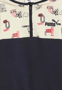 Sudadera con cremallera de Puma que presenta una parte superior crema con estampados gráficos y una parte inferior en azul marino oscuro, mostrando una tela texturizada y colores en contraste.