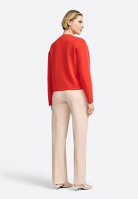 Rode sweatshirt, ronde halslijn, ribbelmanchetten, gedragen met beige broeken. Soepele stof, relaxte pasvorm. Schoeisel met een uniek ontwerp.