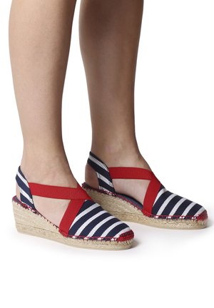 Espadrilky na klínu s pruhovaným horním dílem v námořnické modré a bílé barvě, červenými elastickými pásky a tkanou juty podrážkou s červenými vyšívacími akcenty.