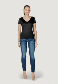 Sort tætsiddende V-udskåret t-shirt parret med mørkeblå slim-fit jeans. T-shirten har korte ærmer, og materialet ser glat ud. Modellen står oprejst.