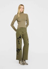 Pulover kaki cu guler ridicat, cu dungi; pantaloni kaki cu picioare largi și broderie neagră florală; ghete gri de gleznă cu imprimeu de șarpe.