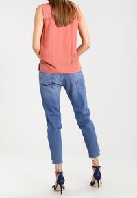 Ärmlös korallblus med spetsdetaljer, blå denimjeans med tapered passform och fransade benslut, tillsammans med marinblå högklackade sandaler.