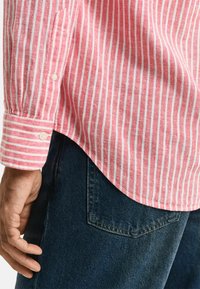 Rood-witte gestreepte blouse met lange mouwen, zachte textuur, knoopmanchetten en op maat gemaakte zoom, gedragen over donkere denimjeans.