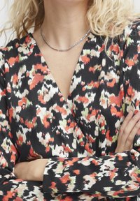 Robe noire portefeuille ornée d'un motif floral abstrait vibrant en rouge, blanc et vert. Elle a des manches longues avec des poignets ajustés et un décolleté en V.