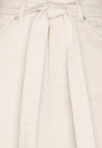 Kermanhalkoinen vyöllinen hame, joka on valmistettu teksturoidusta puuvillasta. Siinä on nauhakiinnitys, siistit linjat ja hienovaraiset ompeluyksityiskohdat.