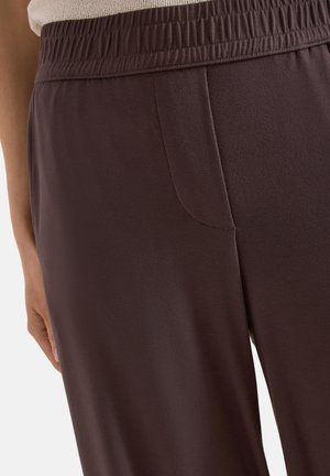 Gros plan sur un pantalon marron foncé à taille élastique avec poche latérale cousue, porté avec un haut en maille beige.