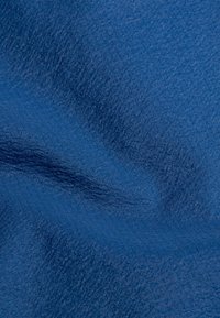 Primo piano di tessuto blu testurizzato con onde sottili e motivi a grana fine visibili su tutta la superficie.