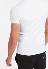 T-shirt bianco a maniche corte con scollatura rotonda, design aderente, texture liscia e linee pulite, abbinato a pantaloni neri con tasca.