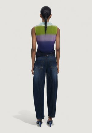 Woman with long braided hair wearing a sleeveless gradient top, wide-leg dark jeans, and blue high-heeled sandals, standing facing away.