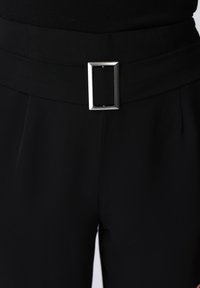 Μαύρο παντελόνι ψηλόμεσο με φαρδιά ζώνη και μεγάλο ορθογώνιο ασημένιο αγκράφα, φορεμένο με μαύρο τοπ.