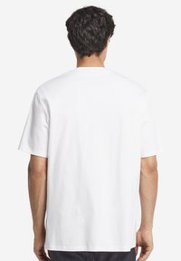 Vit bomulls-T-shirt med korta ärmar, rund halsringning och lös passform. Inga synliga mönster eller logotyper på baksidan. Mjuk yta.