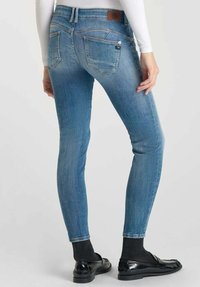 Jean skinny en denim léger, avec une taille haute, deux poches arrière et une étiquette en cuir à l'arrière.