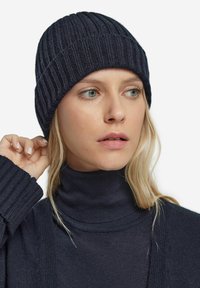 Marine ribbet strikket hue med en tætsiddende pasform. Har en struktureret overflade og en foldet kant, der er parret med en matchende rullekravesweater.