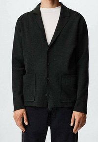 Blazer in lana grigia scuro con rever a punta, due tasche frontali e chiusura a cinque bottoni. Texture liscia, vestibilità sartoriale e design minimalista.