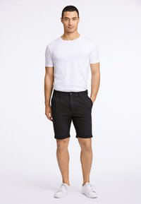Svarta shorts med uppvikta kanter, knappstängning och snedställda fickor. Matchade med en enkel vit t-shirt med korta ärmar och vita sneakers.