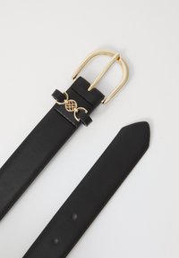 Ceinture en cuir noir avec une boucle en métal doré, dotée d'un détail décoratif en cercle doré. Design de sangle plate avec une pointe effilée.