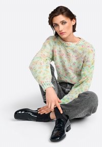 Pull en tricot épais multicolore avec des teintes pastel, manches longues, col rond. Associé à un jean gris et des chaussures noires brillantes.