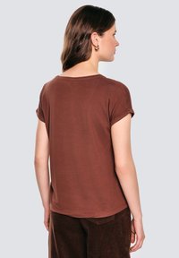 Brązowy t-shirt z krótkim rękawem o luźnym kroju i podwiniętych mankietach, wykonany z miękkiego materiału. Tył ma zaokrąglony dekolt i gładką teksturę.