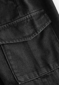 Tissu en denim noir avec une vue rapprochée d'une poche à rabat, présentant des coutures visibles et un motif de tissage texturé, mettant en avant la durabilité.
