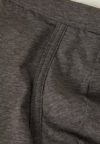 Grauer Stoff mit einer weichen Textur, der Nähte und Stichdetails aufweist und ein leicht zerknittertes Aussehen zeigt.
