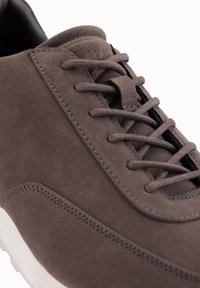 Bruna mockasiner i mocka med rund tå, texturerad yta och förstärkt sömnad. Har platta snören och en vit gummisula.