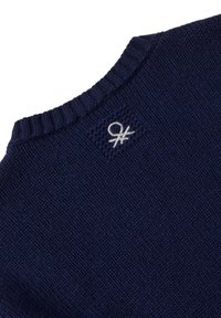 Primo piano del colletto di un maglione lavorato a maglia blu navy con un piccolo logo ricamato bianco vicino al colletto.