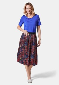 Haut à manches courtes bleu associé à une jupe à taille élastique noire présentant des rayures rouges, bleues et jaunes ainsi que des motifs abstraits. Chaussures blanches.