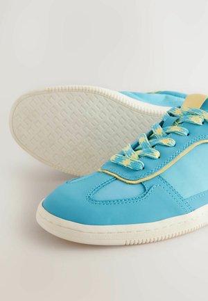 Blå sneakers tillverkade av slät syntetiskt material, med texturerade vita sulor, kontrasterande gula detaljer och blå mönstrade snören.