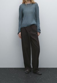 Blue knit sweater with a relaxed fit, paired with high-waisted black wide-leg trousers. Black mesh slip-on shoes with circular cutouts.