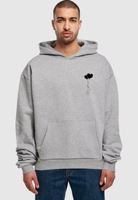 Grauer Baumwoll-Hoodie mit einer Fronttasche, auf der Brust mit einer schwarzen Grafik einer Figur, die zwei schwarze Ballons hält. Lässiger Schnitt, Kapuze mit Kordelzug.