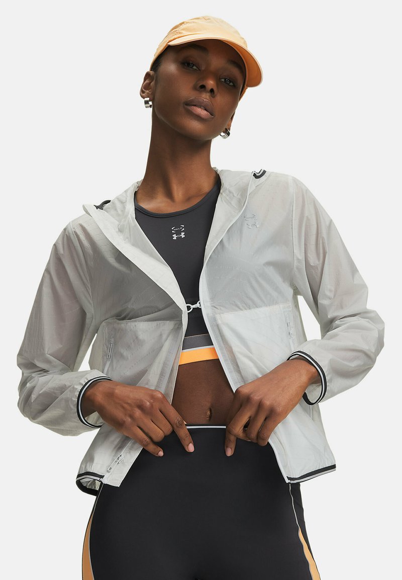 Lekka, przezroczysta kurtka z kapturem, zapinana na zamek błyskawiczny, z czarnymi akcentami. Noszona na ciemnym topie na ramiączkach i czarnych leginsach z wysokim stanem.