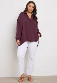 Blusa bordeaux botton-up con colletto, maniche lunghe e tasca; abbinata a pantaloni bianchi a gamba dritta e sandali marroni.