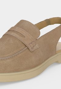 Mocassin en daim marron clair avec bride arrière, couture style mocassin et semelle en caoutchouc beige.