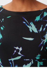 Nacken und Oberkörper tragen ein schwarzes Top aus Stoff mit abstrakten Pinselstrichmustern in Blau, Türkis und Lila.