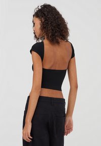 Top nero corto con maniche corte a cappuccio e design aperto sulla schiena, abbinato a pantaloni neri con vita alta. Tessuto morbido.