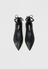 Μαύρα επίπεδα παπούτσια μυτερά με μεταλλικές τρουκς, με λεπτομέρειες κορδονιών στον αστράγαλο. Κατασκευασμένα από λείο δερμάτινο υλικό.