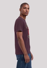 Maroon cotton t-shirt with a round neckline, short sleeves, and a graphic print featuring lips and text on the front. Paired with blue jeans.