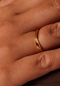Gouden ring met een gladde, gepolijste oppervlakte, snug passend op een hand, met een taps toelopend ontwerp en subtiele reflecterende accenten.