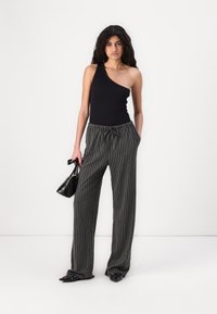 Haut noir à une épaule associé à un pantalon gris rayé et ample. Le pantalon possède une ceinture élastique et un cordon de serrage. Sac à main noir et chaussures.
