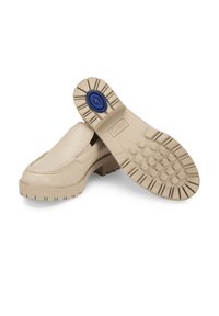 Beige slip-on shoes with a textured upper and a rugged, hexagonal patterned rubber outsole featuring a blue accent on the heel.
