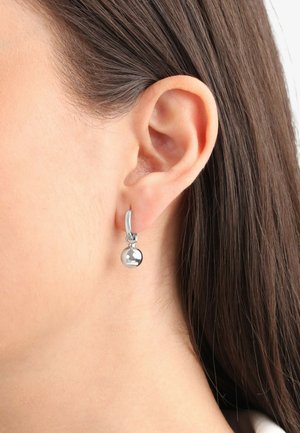 Pendientes de aro de plata con un pequeño acento esférico brillante. El material es metal pulido, creando una superficie reflectante.