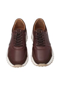 Para brązowych skórzanych sneakerów z ciemnymi sznurowadłami i białymi gumowymi podeszwami, widziana z góry na białym tle.