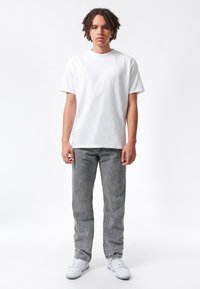 T-shirt bianca in cotone con colletto rotondo, abbinata a jeans grigi con finitura testurizzata, indossata con sneakers bianche.