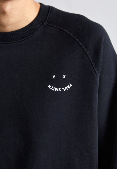 Svart hettegenser med rund hals og raglanermer, med hvit brodert tekst "PAUL SMITH" og et smilendesign på brystet.