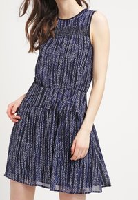 Marinefarbendes ärmelloses Kleid mit strukturiertem Oberteil, fließendem Rock und vertikalem Muster aus blauen, weißen und lila Linien.