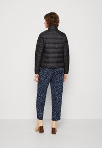 Giacca a vento nera con cuciture orizzontali, abbinata a pantaloni navy con pois. Il modello indossa stivaletti con tacco a blocco beige.