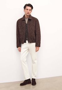 Dark brown textured jacket with a collar, worn over a gray button-up shirt and white pants, paired with dark brown ankle boots.